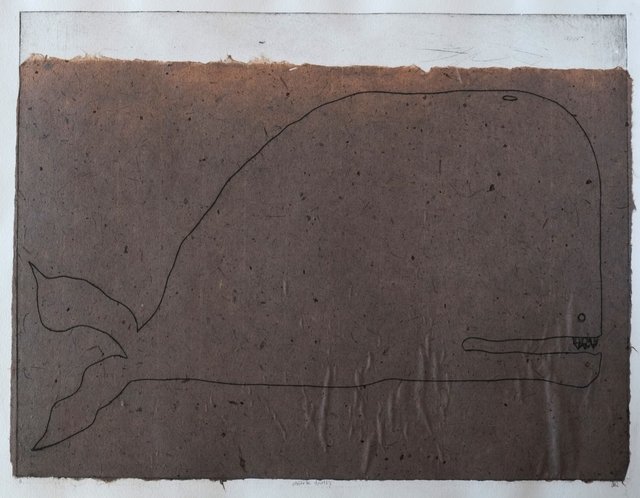 Intaglio print of a whale rendered in simple contour lines on dark brown handmade paper, with small crystalline teeth visible in its open jaw and a forked tail at left.