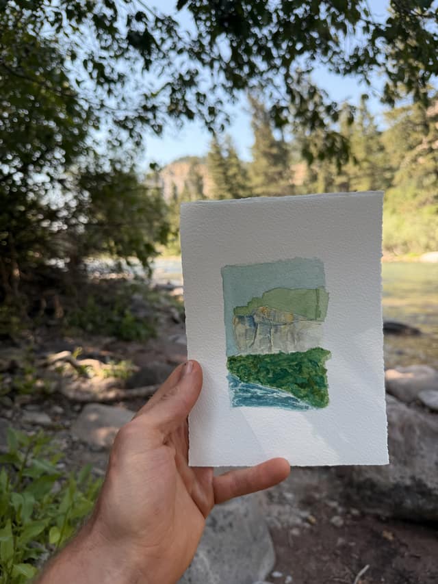 Small gouache and watercolour in a cream mat: pale grey-gold limestone bluffs under a green-blue sky, a band of dense green trees below, and blue river water along the bottom edge. Titled in pencil, "storm castle bluffs".