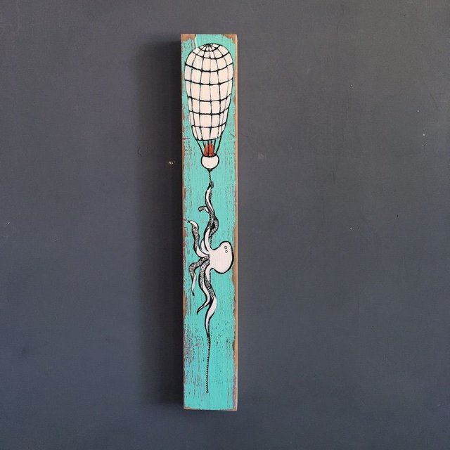 Mixed media painting on a tall narrow piece of found wood showing a white octopus dangling from a hand-sewn hot air balloon on a turquoise background.