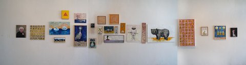 Installation view of a long white gallery wall hung with a single band of paintings and works on paper, including a portrait, a heron, an owl, a rhinoceros, a grid of small circles and several panels of repeated pattern.