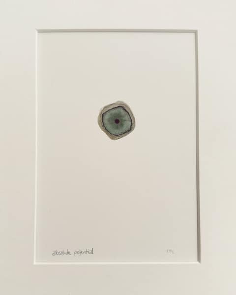 Small gouache and watercolour painting in a white mat: a single rounded, cell-like form in grey-green with a darker ring and a dark centre, alone in the middle of a wide white field. Titled in pencil below, "absolute potential".